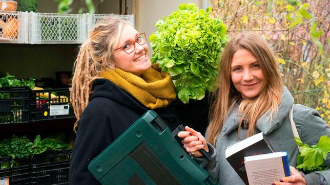 Jana (r) steht zusammen mit Tine von foodsharing vor einem Stapel Kisten mit Lebensmitteln und beschäftigt sich mit dem Thema "Teilen statt kaufen - Gut für Geldbeutel und Umwelt?!"