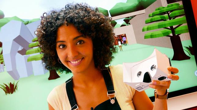 Moderatorin Siham El-Maimouni steht vor einer 3D-Animation und hält eine VR-Brille in der Hand.