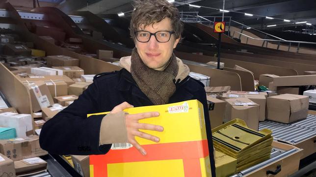 Robert steht mit einem Paket in einem Paketverteilzentrum.