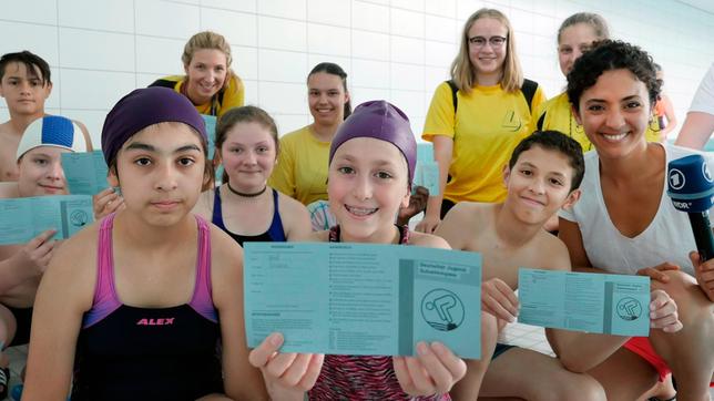 Siham (r) gemeinsam mit den Schülern der Schwimm-AG des Leibniz-Gymnasiums Essen. Einige der Schüler halten ihren Jugend-Schwimmpass in die Kamera.