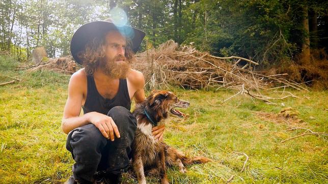 Wanderschäfer Sven hockt mit seiner Hündin Bebi im Grünen.