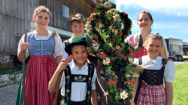 In den Ferien helfen Kinder aus der Nähe auf der Alpe. Hannes (vorne links), Magdalena (vorne rechts) und Jona (Mitte hinten) und zwei Helferinnen stehen neben der geschmückten Kuh „Lena“.