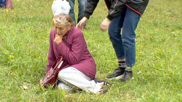 Eine ältere Frau sitzt verzweifelt im Gras.