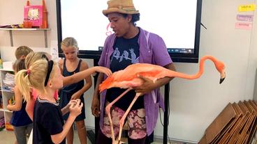 Eine Frau hält einen Flamingo auf dem Arm, umringt von Kindern.