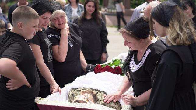 Angehörige eines toten Soldaten stehen um seinen Leichnam im offenen Sarg.