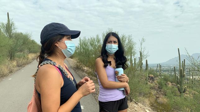 Zwei junge Frauen mit Masken unterhalten sich. 