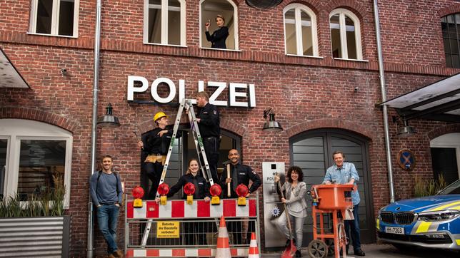 Die Bauarbeiten sind beendet! Das Team vom Großstadtrevier vor dem neuen Revier: v.l.n.r. Piet Wellbrook (Peter Fieseler), Daniel Schirmer (Sven Fricke), Nina Sieveking (Wanda Perdelwitz), Hannes Krabbe (Marc Zwinz), Lukas Petersen (Patrick Abozen), Harry Möller (Maria Ketikidou) und Dirk Matthies (Jan Fedder). Kommissariatsleiterin Frau Küppers (Saskia Fischer, oben) hat alles im Blick.