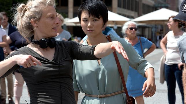 Bild: rbb/die film gmbh/Volker Roloff Ein belebter Platz mitten in der Stadt, 12 Uhr mittags. Gerade winkt die Studentin Mina Jiang (Yun Huang) noch ihrer Kommilitonin Luise (Paula Kroh) von weitem zu, als sie plötzlich tot zusammenbricht. Ein Schuss in den Hinterkopf führt die Kommissare Rubin (Meret Becker) und Karow (Mark Waschke) in die historische Mitte Berlins. - Brigitte Bertele (Regie, links) mit Yun Huang (Rolle Mina Jiang, rechts).
