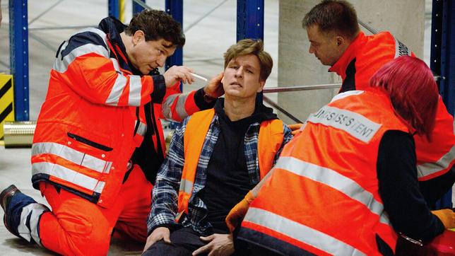 Bild: ARD/Volker Roloff Christian (Francis Fulton-Smith) ist als Notarzt vor Ort: Boris Kehr (Jürgen Klein) wurde von einer herabfallenden Pallette verletzt (mit Komparsen).