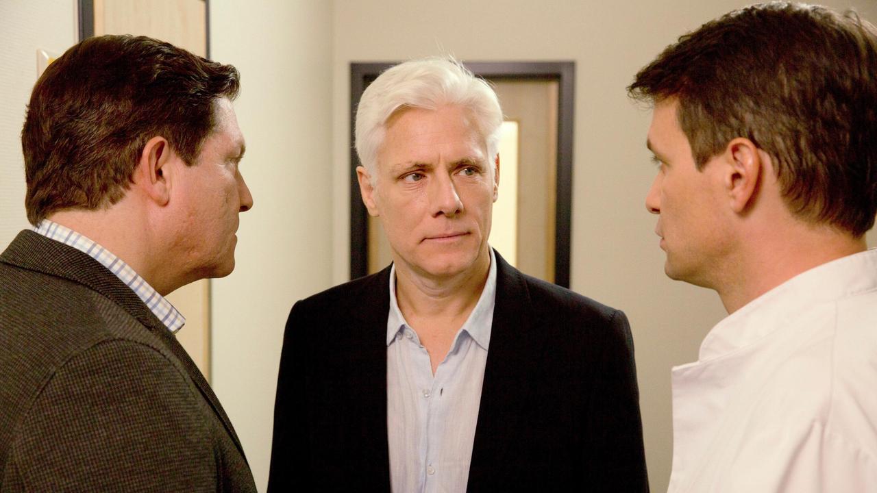 Christian (Francis Fulton-Smith) und Michael (Luca Zamperoni) informieren Georg Schneider (Philippe Brenninkmeyer) über einen erneuten Fieberschub bei seiner Frau.