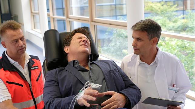 Bild: ARD/Jacqueline Krause-Burberg Christian (Francis Fulton-Smith, M. mit Komparse) wird mit starken Schmerzen ins Krankenhaus eingeliefert. Michael (Luca Zamperoni) kümmert sich um ihn.