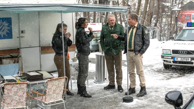 Das Team berät über den aktuellen Fall vor dem provisorischen Wohnwagen-Revier, während der Verdächtige mit seinem Anwalt spricht. V.l.n.r. Rebecca (Jeanne Goursaud), Sabine Kaiser (Katharina Müller-Elmau), Girwidz (Michael Brandner), Hubert (Christian Tramitz).