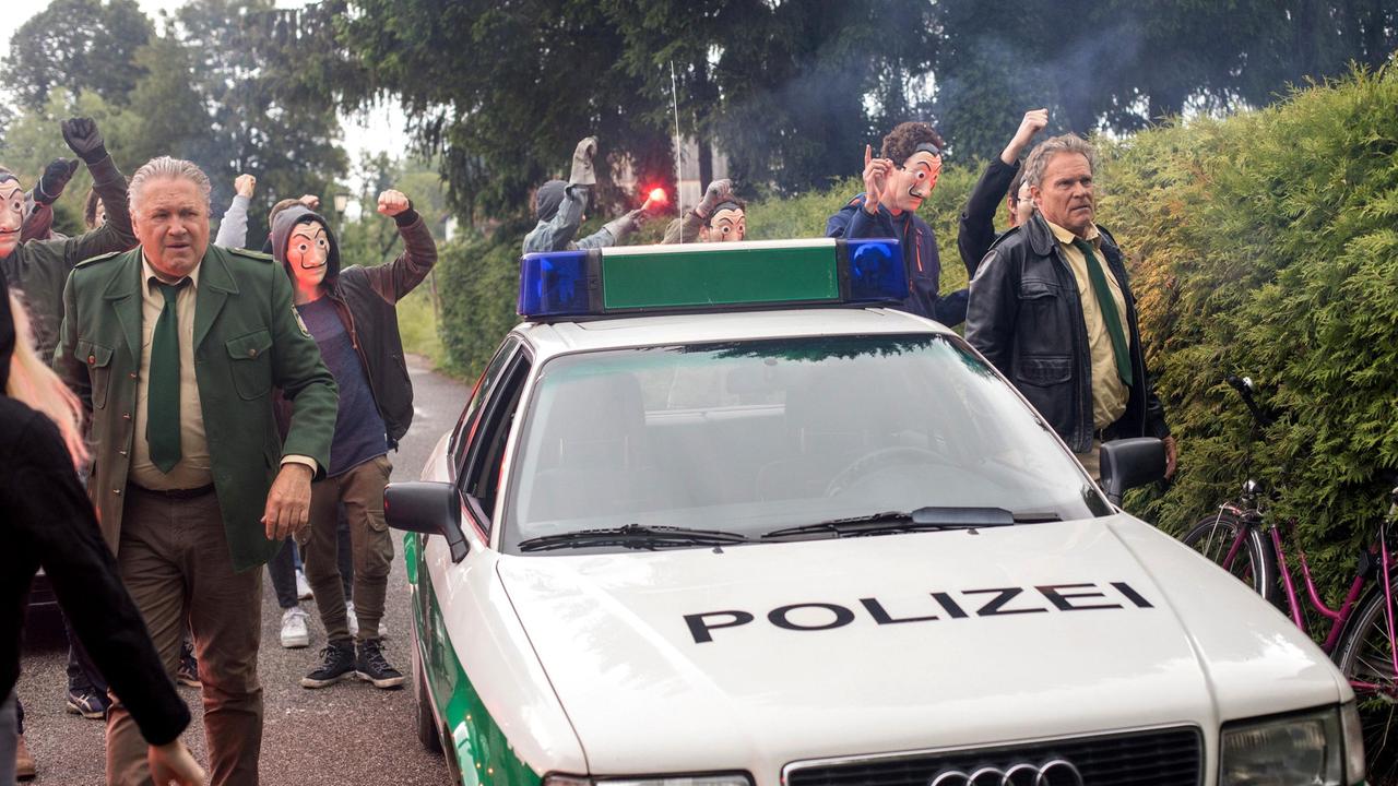 Hubert (Christian Tramitz) und Girwidz (Michael Brandner) werden zu einem Einsatz gerufen- eine wütende Gruppe von Demonstranten (Komparsen) hat sich vor einem Haus versammelt.