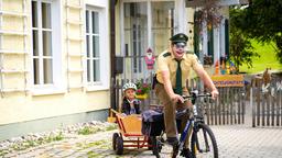 Riedl (Paul Sedlmeir) bemerkt nicht, dass er aussieht wie ein Clown und macht sich mit Lina (Carla Graßl) im Bollerwagen auf den Weg zum Revier.