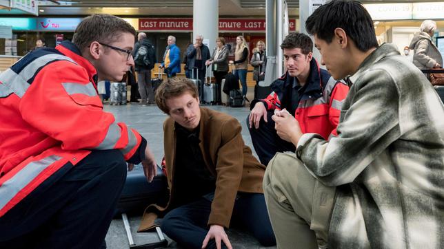 Bei ihrem Flughafeneinsatz kümmern sich Ben Ahlbeck (Philipp Danne) und Elias Bähr (Stefan Ruppe) um die beiden zerstrittenen Kollegen und Freunde Nick Jauer (Xidou Zhao) und Marvin Verl (Joscha Eißen, 2.v.l. mit Kompars:innen, h.).