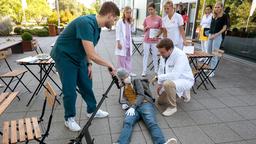 Dr. Marc Lindner (Christian Beermann) und Mikko Rantala (Luan Gummich) sitzen in der Cafeteria, als Joshy Binder (Laurids Schürmann) mit seinem Roller stürzt und sich verletzt (mit Kompars:innen, h.).