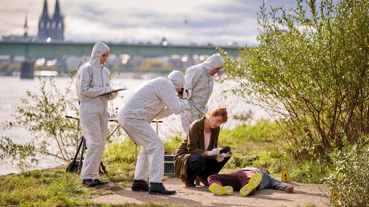 Dr. Schmidt (Helene Grass) weist die Kollegen (Komparsen) in den Tatort ein.