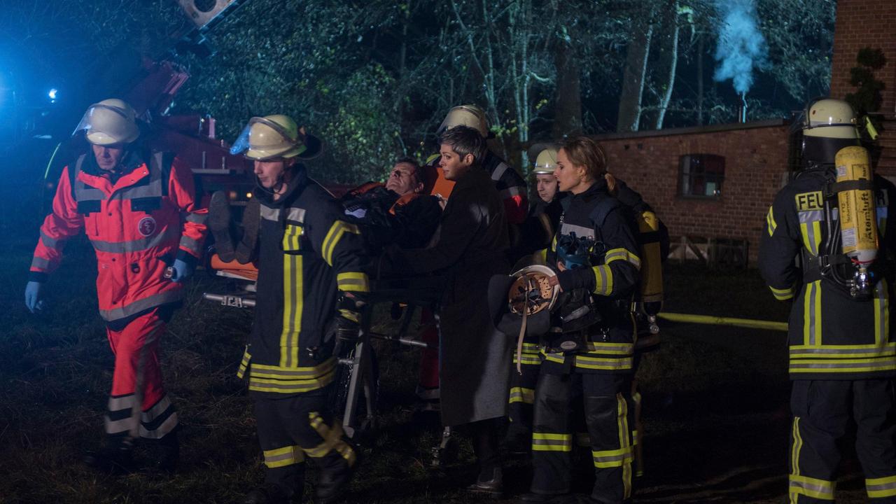 Der Feuerwehr gelingt es, Gunter (Hermann Toelcke) bewusstlos und schwer verletzt aus der brennenden Kulturscheune zu bergen. Sydney (Cheryl Shepard) bangt um das Leben ihres Bruders (mit Hedi Honert, 2.v.r. und Komparsen).