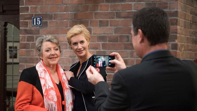 Simone (Dorothea Schenck) nutzt die Begegnung mit der Kunstmäzenin Frederike Prinzessin zu Lüdecke (Marie-Luise Marjan), um daraus Profit für ihren Wahlkampf zu schlagen (mit Komparse).