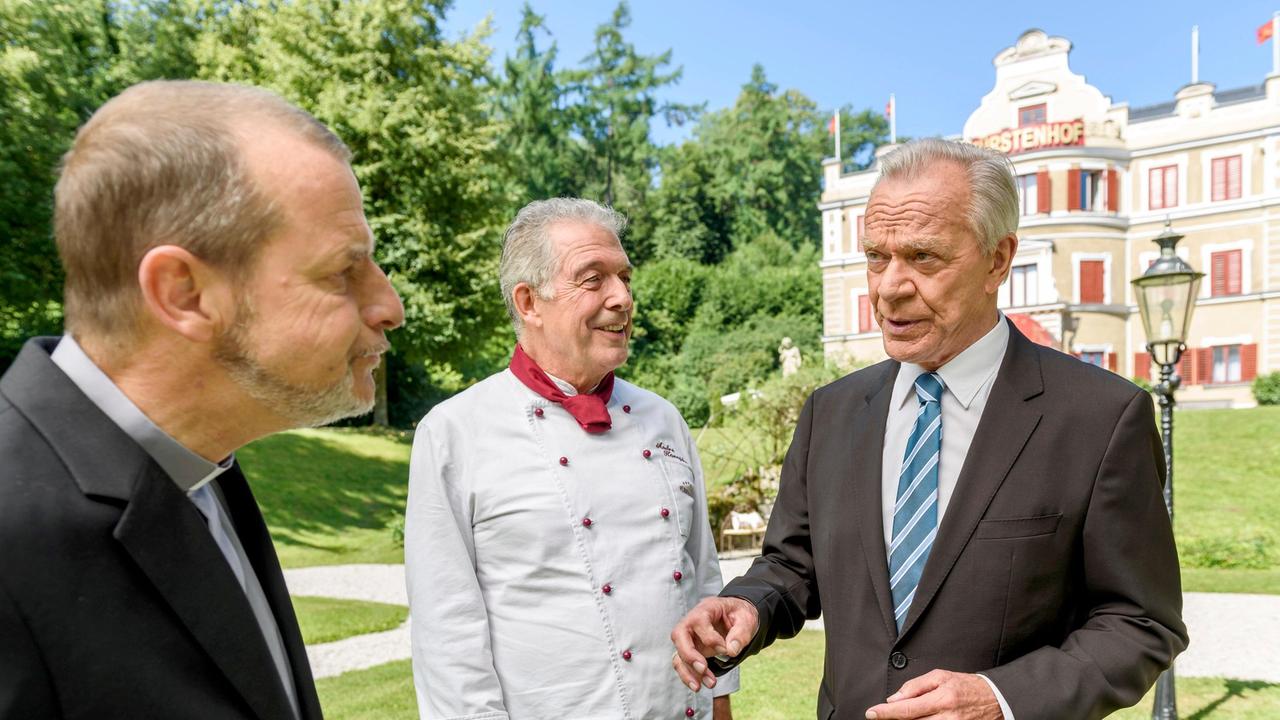 André (Joachim Lätsch) amüsiert sich über Werners (Dirk Galuba) vergebliche Versuche, Pfarrer Rimpel (Christian Buse) umzustimmen.