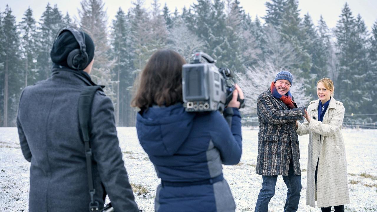 André (Joachim Lätsch) stört Rosalies (Natalie Alison) Interview (mit Komparsen).