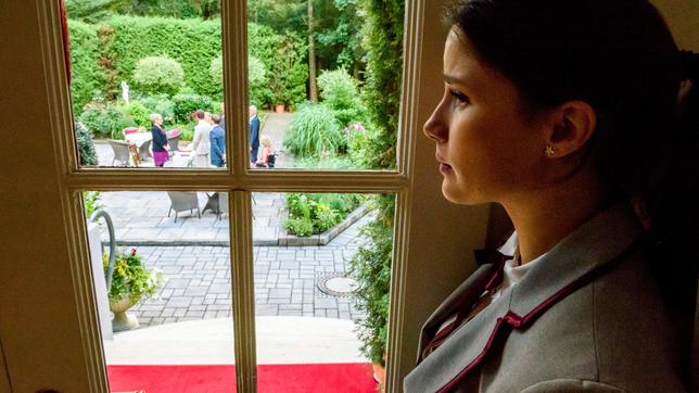 Clara steht am Fenster und blickt nach draußen.