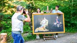 Joshua (Julian Schneider) und Denise (Helen Barke) posieren mit dem Bild von Dora und George vor dem Fotograf (Komparse).