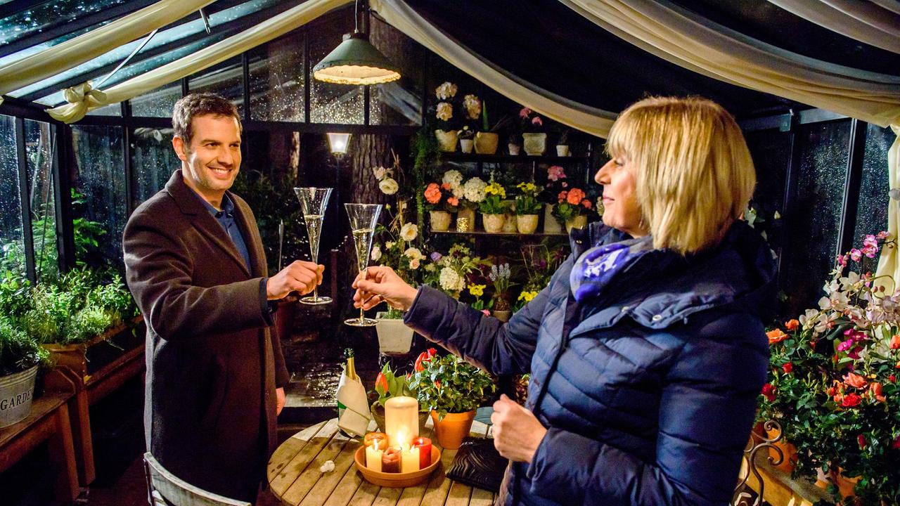 Nils (Florian Stadler) und Charlotte (Mona Seefried) treffen sich mit einer Flasche Champagner im Gewächshaus und tanzen spontan zusammen.