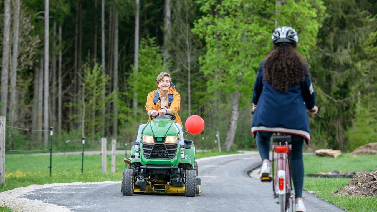 Shirin (Merve Çakır) wird von Gerry (Johannes Huth), der ihr auf einem Rasenmäher entgegenkommt, abgelenkt.